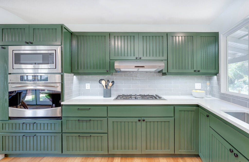 Modern kitchen remodel with green cabinets and brushed stainless steel appliances.